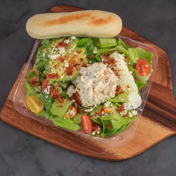 Chilly Jilly'z cafe salad with chicken, avocado, bacon, tomatoes, and feta cheese, served with a breadstick.