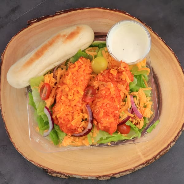Chilly Jilly'z buffalo chicken salad with breadstick and ranch dressing on a wooden board.