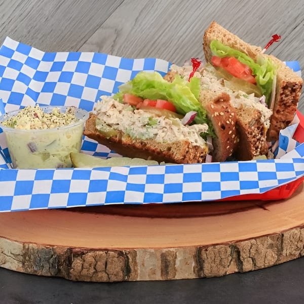Chicken salad sandwich with lettuce, tomato, and a side of potato salad in a blue checkered basket.