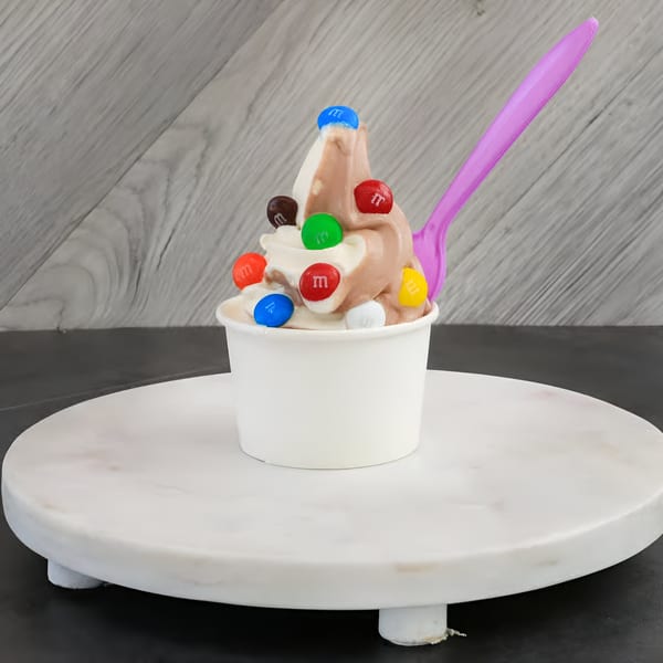 Swirled chocolate and vanilla frozen yogurt with colorful M&M's and a pink spoon in a white cup.